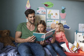 父亲和他的小女儿们一起坐在孩子们房间的床上看书图片素材