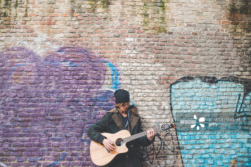 Musician playing guitar by canal wall, Milan, Italy圖片素材