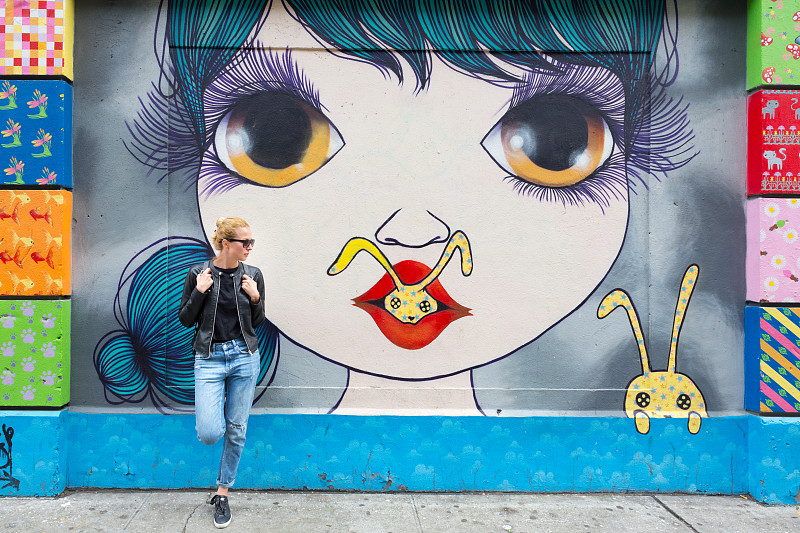 美國紐約，一名女子靠在彩色涂鴉墻上講著智能手機。圖片素材
