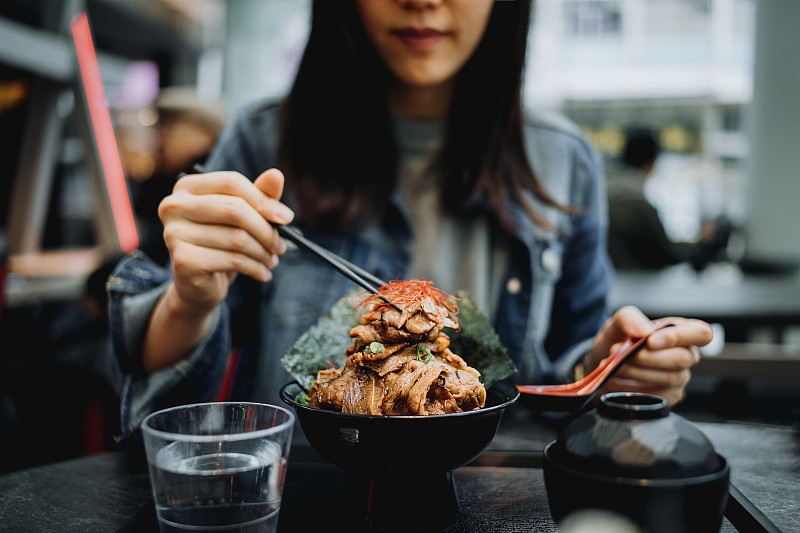 年輕的亞洲婦女在日本餐館愉快地用筷子吃烤牛肉飯碗圖片素材