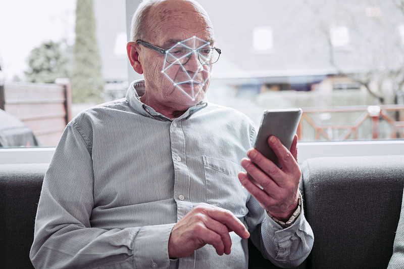 老人拿著手機，手機應用掃描他的臉圖片素材