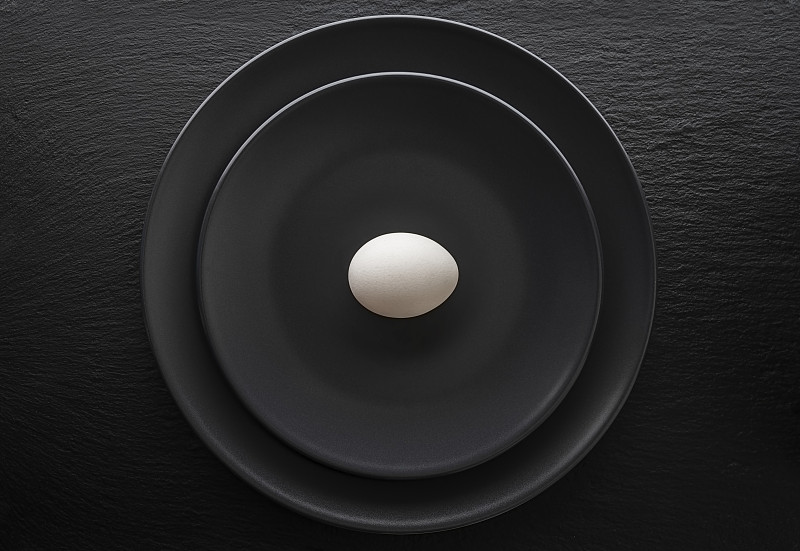 一個雞蛋放在一個黑色的盤子里。這個盤子放在一個黑色的石板盤子上。圖片素材