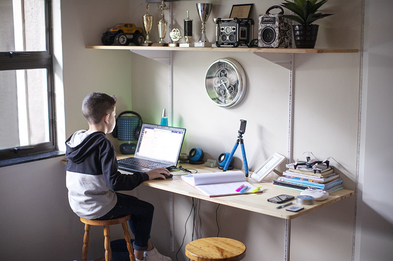 一個九歲的男孩在家里用筆記本電腦做作業。圖片素材