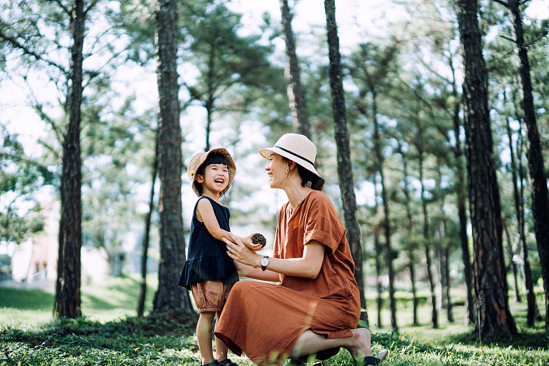 可爱的年轻亚洲母亲放松与她的小女儿在树林里，聊天和愉快的微笑，对着美丽的阳光。母女之间的珍贵时刻。家庭生活方式。亲情关爱。探索自然和户外乐趣图片下载