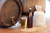 啤酒厂，饮料和酒精概念-接近老啤酒桶，玻璃，瓶子和麦芽袋在木桌上图片素材
