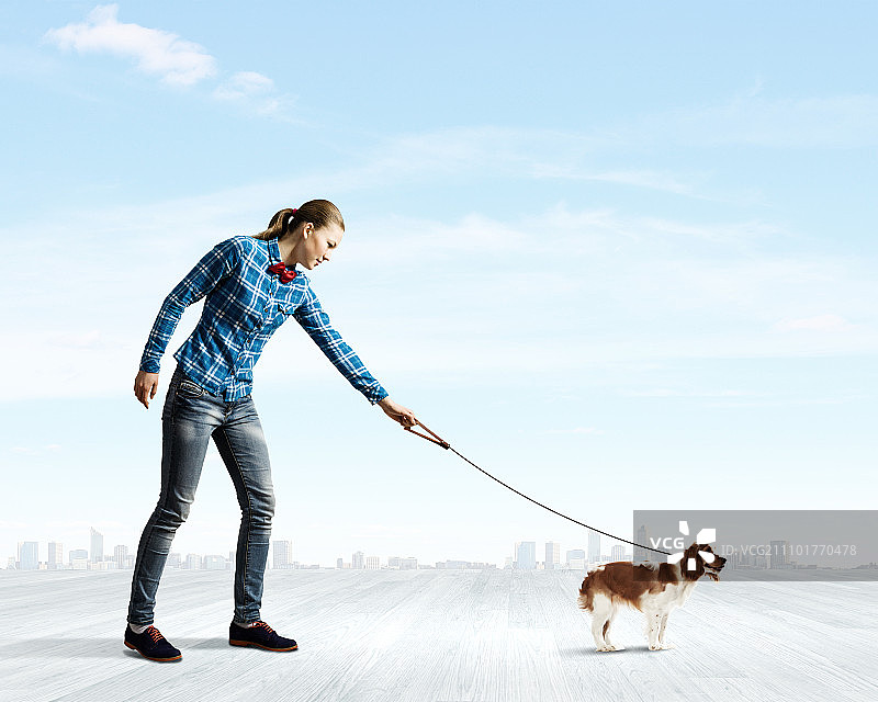 女人与狗。年轻女子在不经意间牵着狗散步图片素材