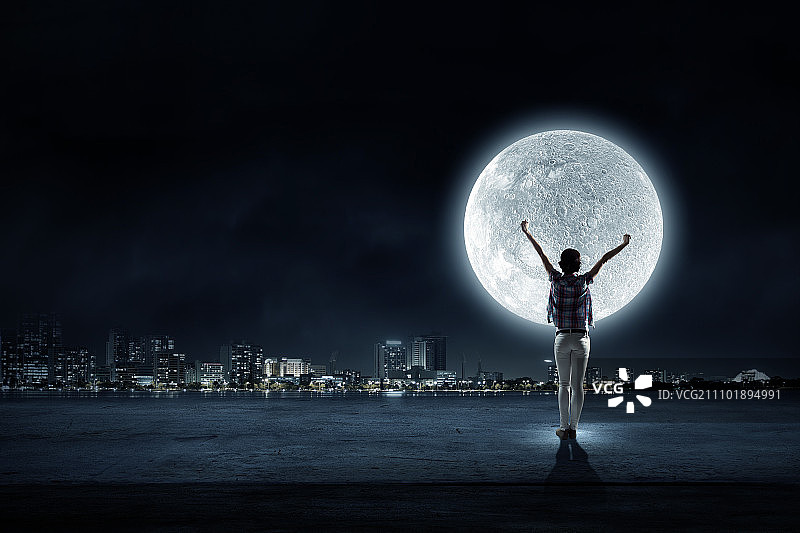 满月。后视图的年轻女子与手向上看在天空中的月亮图片素材
