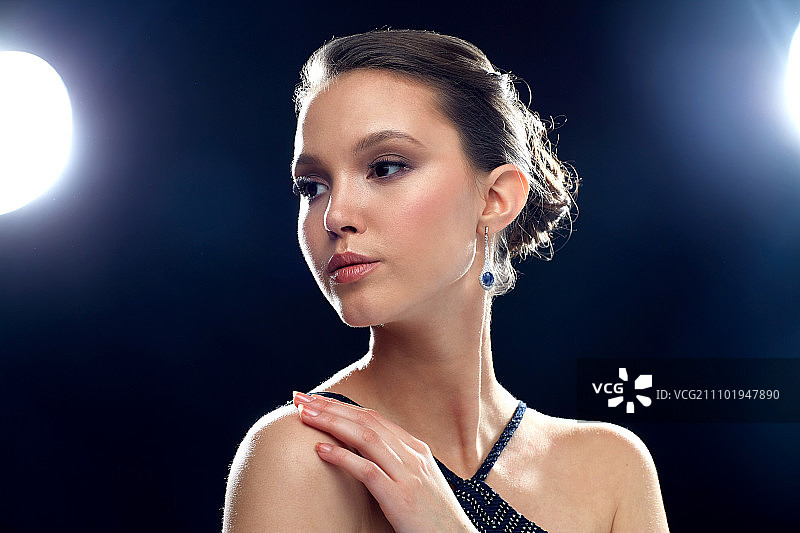 美丽，珠宝，人和奢侈品的概念-美丽的年轻亚洲女性与耳环在黑色的背景和聚光灯图片素材