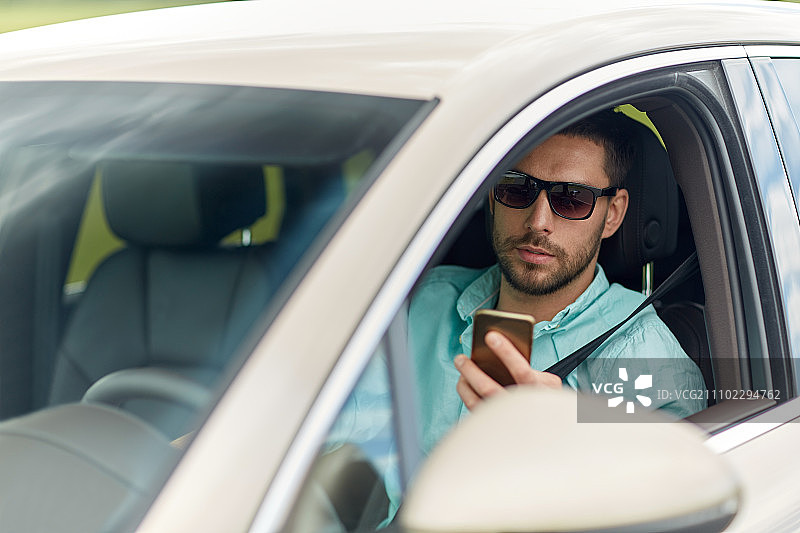 公路旅行，交通，旅行，技术和人的概念-男人在太阳镜驾驶汽车与智能手机图片素材