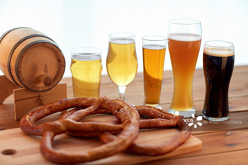啤酒厂，饮料和食品概念-接近不同的啤酒杯，木桶和椒盐卷饼在桌子上图片素材