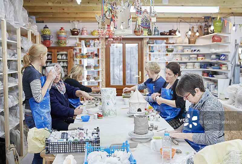 一群人坐在陶器作坊的工作台上，手工制作陶器。喝着茶的女人。图片素材