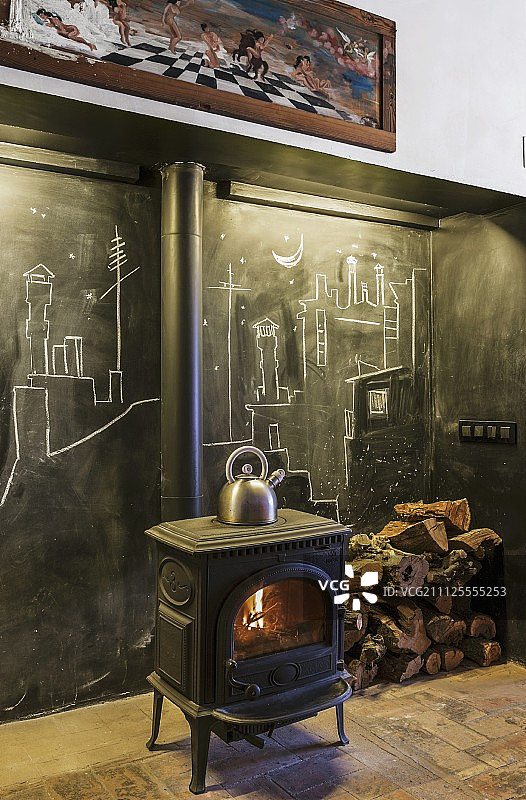燃烧木材的火炉在黑板墙前面，粉笔画和堆放的柴火在乡村的气氛图片素材