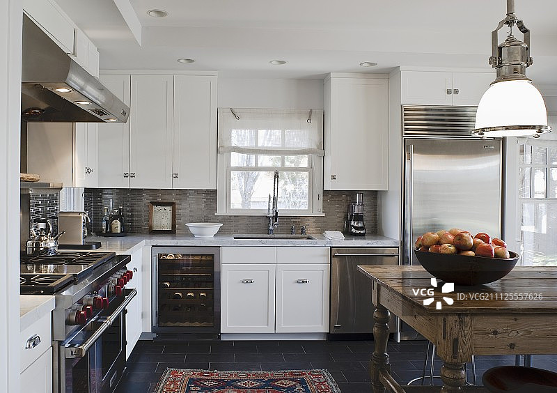 乡村别墅厨房配有白色的橱柜门，质朴的桌子和老式的工业吊灯图片素材