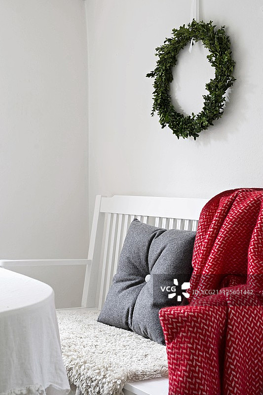 墙上挂着圣诞花环，白色的长凳上放着灰色的毛毡垫和红白相间的毛毯图片素材