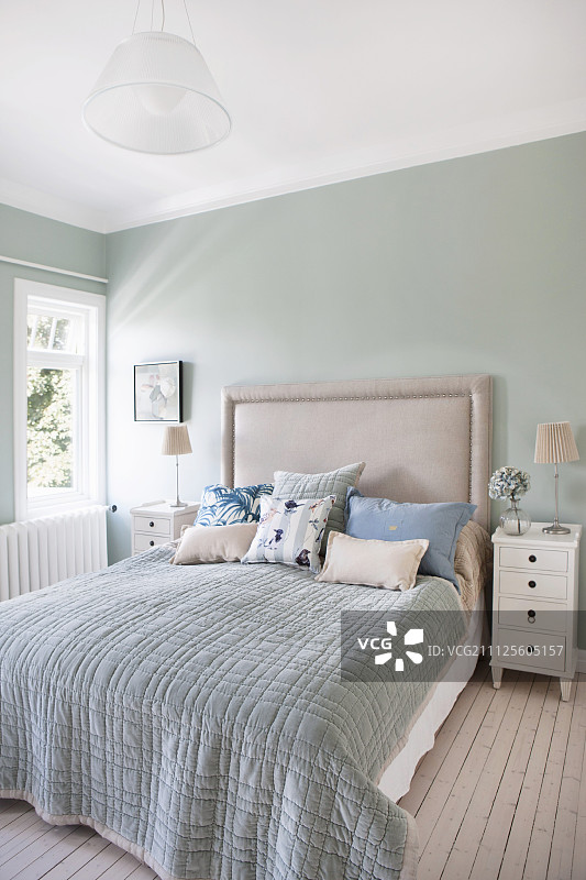 卧室里有双人床和软垫床头板，靠在淡绿色墙壁上图片素材