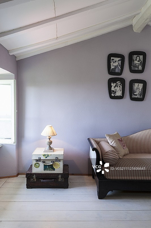 台灯放在一堆古董行李箱上，旁边是古董沙发，靠在淡紫色的墙上图片素材