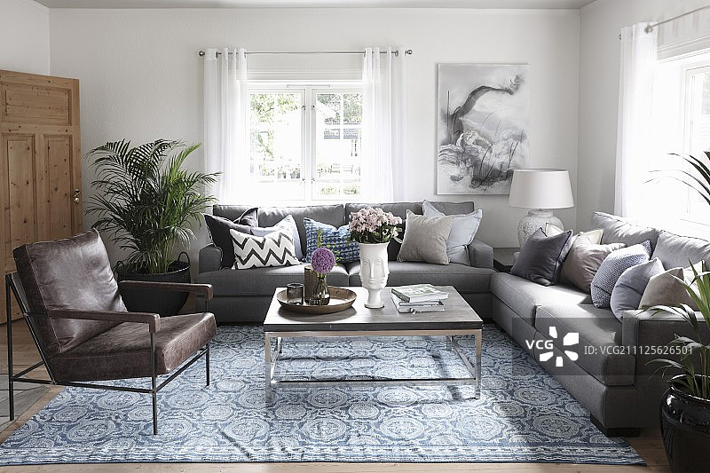 皮革扶手椅和沙发周围的现代咖啡桌和图案地毯在乡村客厅图片素材