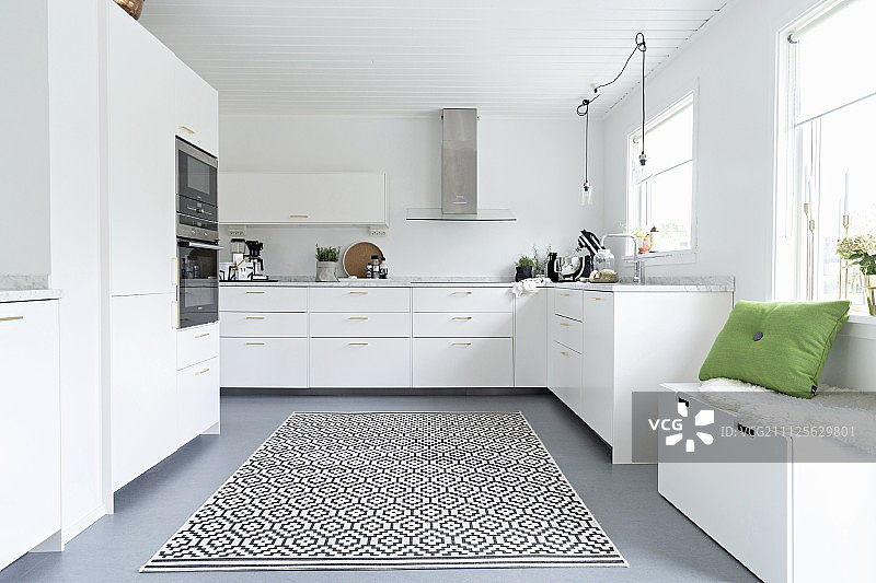 窗户下的储物凳和带有图形图案的地毯在优雅的白色配备厨房图片素材