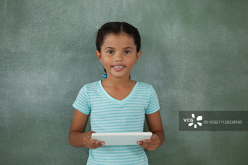 年轻的女孩拿着数字平板电脑对着黑板图片素材