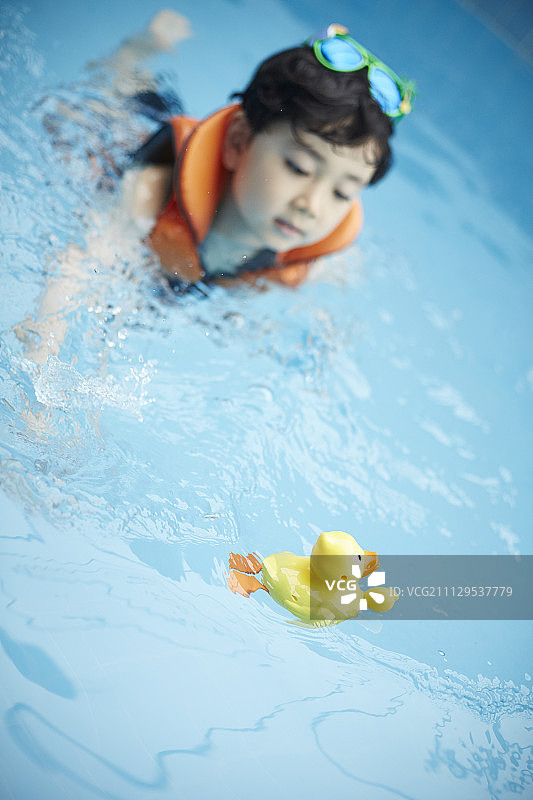 男孩穿着救生衣和鸭子形状的玩具在游泳池里图片素材