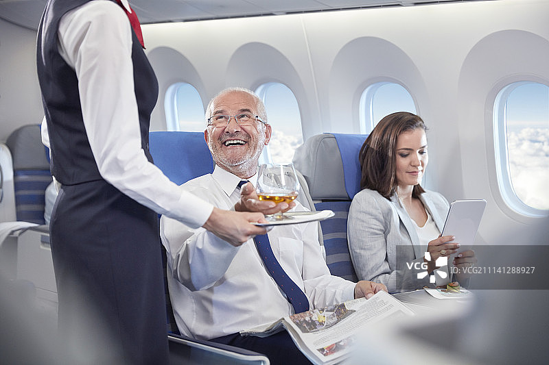 空姐在飞机头等舱为微笑的商人提供威士忌图片素材