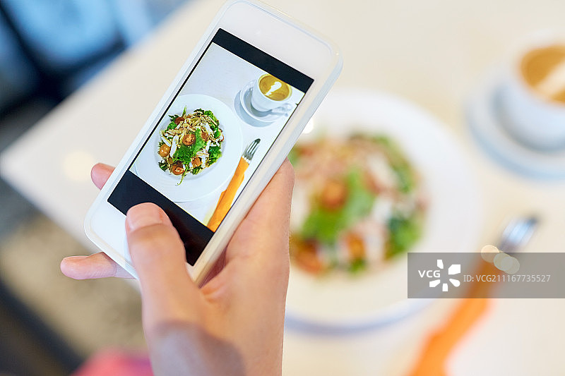 食物，技术，饮食和人的概念-近距离的女人的手与智能手机拍摄沙拉在餐厅。用智能手机拍摄餐厅食物图片素材