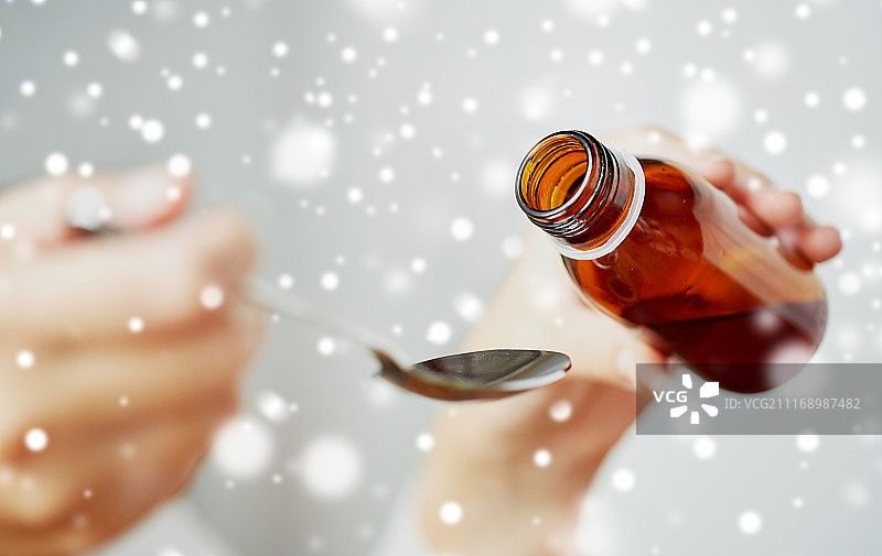 医疗保健，人和医学概念-妇女倒药或退热糖浆从瓶子到勺子在雪。把药从瓶子倒到勺子里的女人图片素材