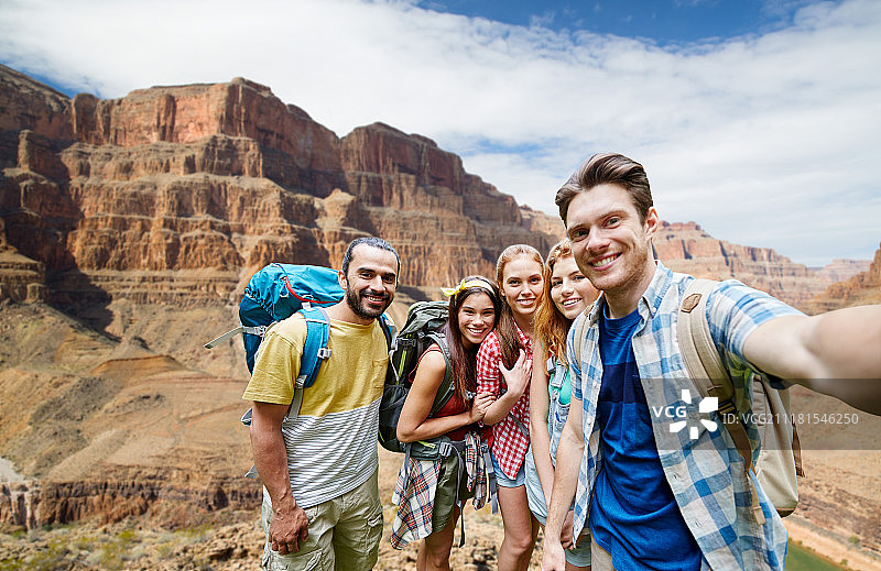 旅游、旅游和科技概念——一群微笑的朋友或旅行者背着背包在大峡谷国家公园的岩石上自拍。快乐的旅行者在大峡谷自拍。快乐的旅行者在大峡谷自拍图片素材