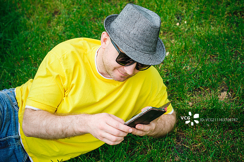 戴着墨镜和帽子的男人躺在草地上用智能手机图片素材