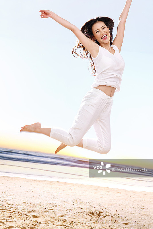 快乐的年轻女性在海边跳跃图片素材