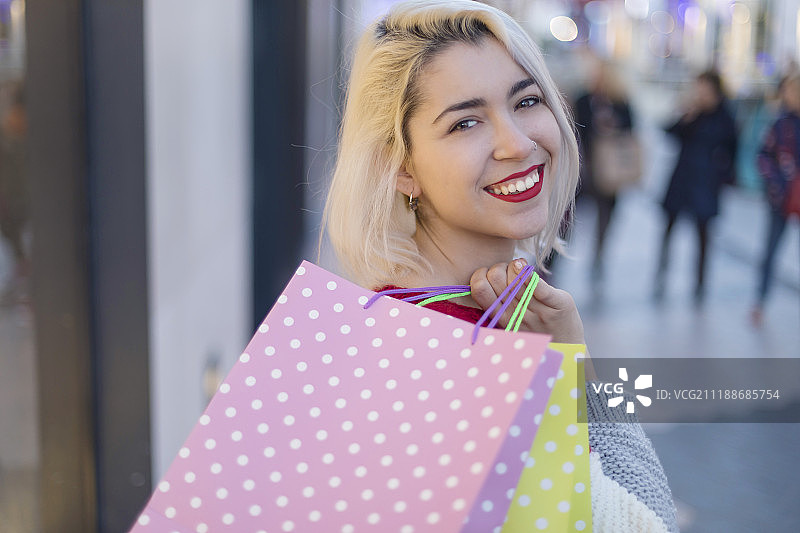 一个微笑的年轻女子站着，拿着商店的袋子图片素材