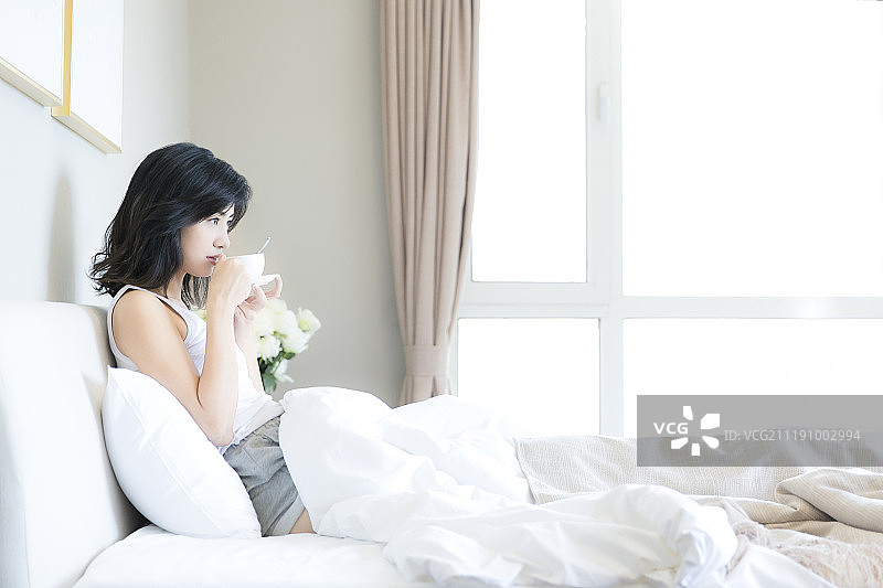 年轻女子在卧室床上喝咖啡图片素材