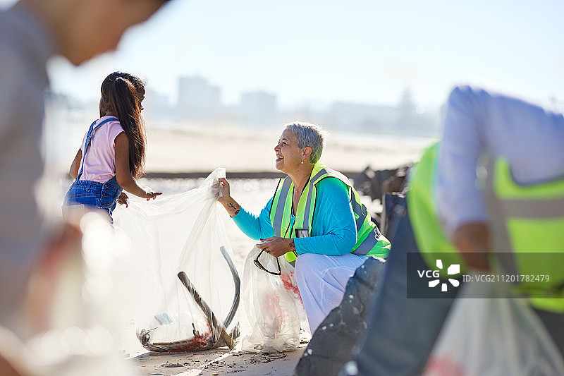 年长的妇女和女孩志愿者在阳光明媚的海滩上清理垃圾图片素材
