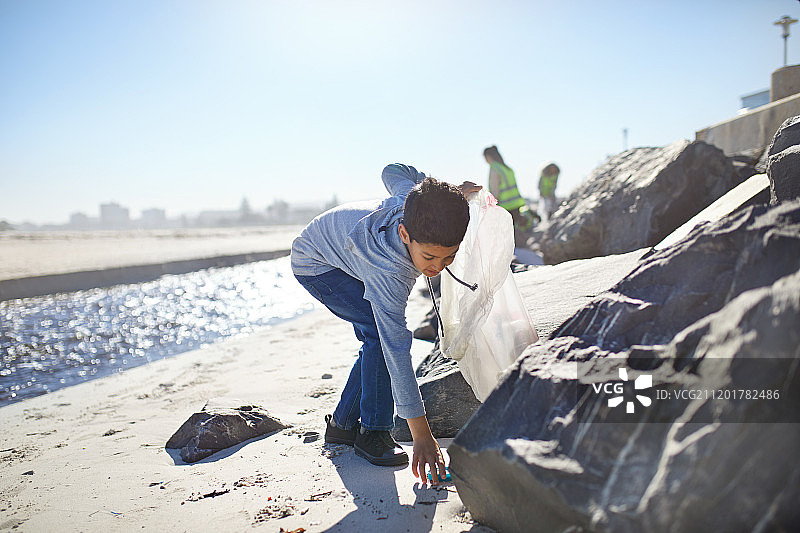 男孩志愿者在阳光明媚的海滩上捡垃圾图片素材