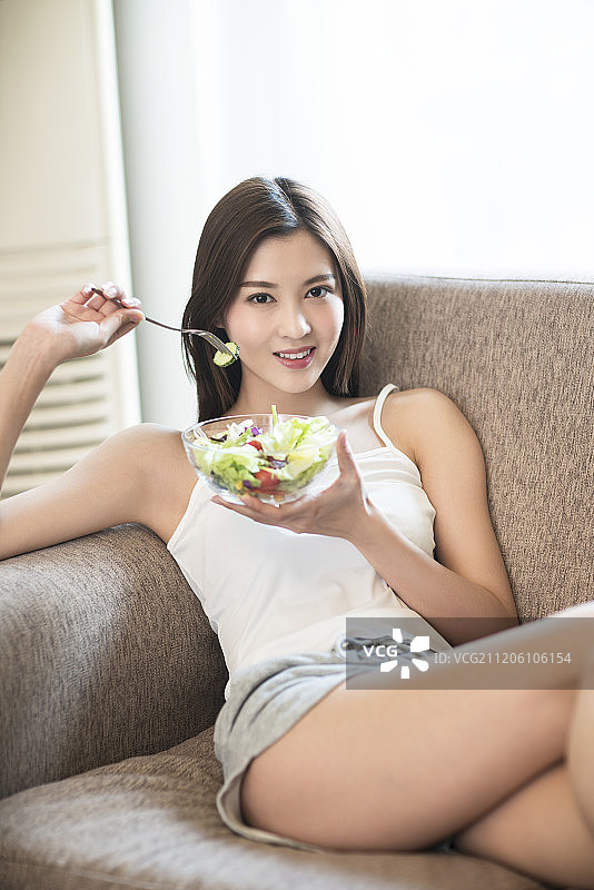 年轻女子在沙发上吃蔬菜沙拉图片素材