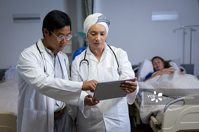 多民族医生讨论数字平板电脑，而高加索女性病人躺在床上的背景在医院诊所图片素材