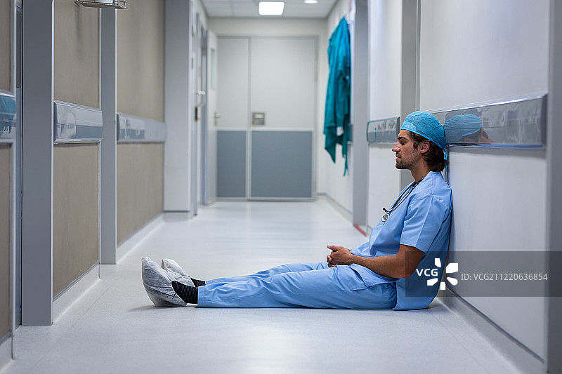 一位白人男性外科医生坐在走廊里，靠在医院的墙上图片素材