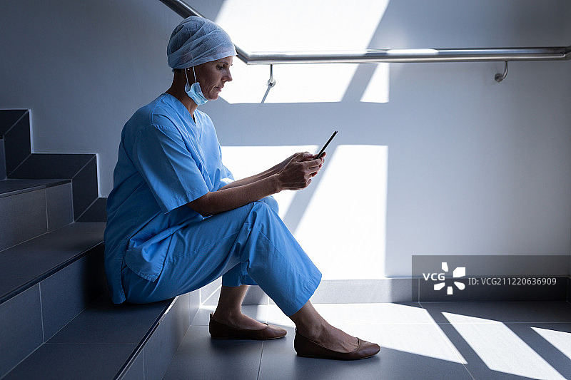 一位白人女外科医生坐在医院楼梯上使用手机的侧视图图片素材