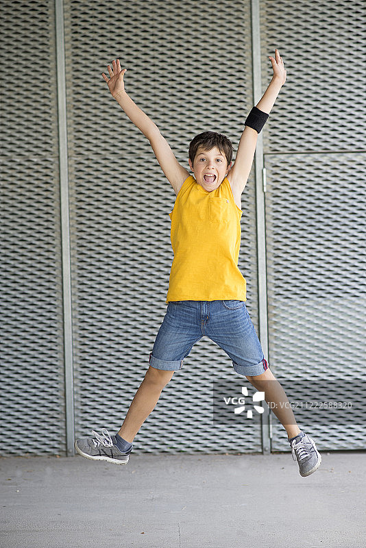 正面的一个微笑的愉快的男孩跳跃，而双臂举起在户外在一个光明的日子图片素材