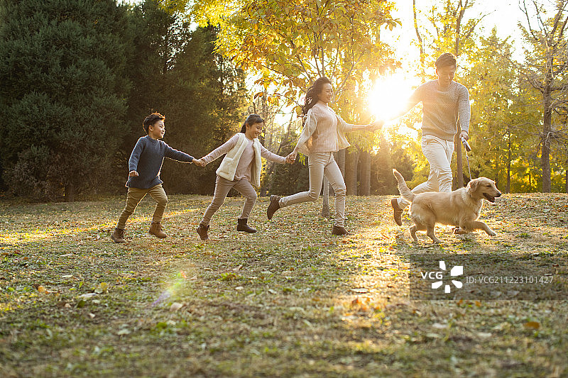 快乐的年轻家庭和狗在秋日的树林里图片素材