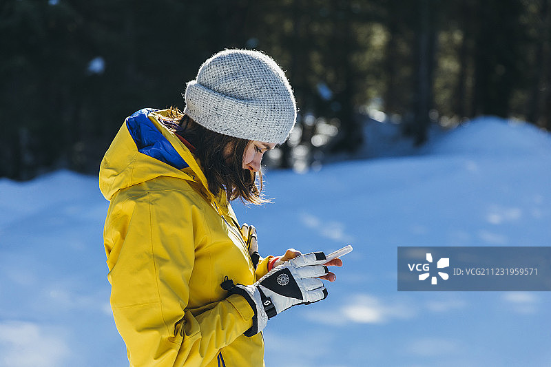 侧视图拍摄的年轻女子在室外使用手机的冬天，惠斯勒，不列颠哥伦比亚省，加拿大图片素材