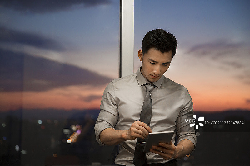 一个成功青年男商务人士站在办公大厦玻璃窗前使用平板电脑工作图片素材