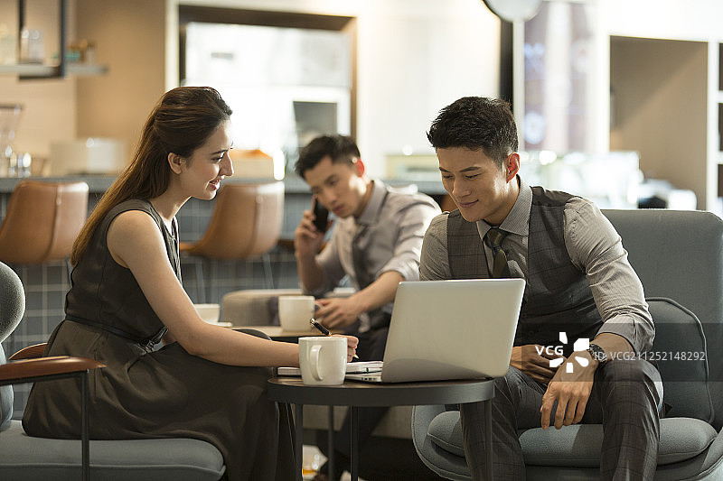 青年商务男子和青年女助理在办公室休闲区喝咖啡使用笔记本电脑探讨沟通工作图片素材