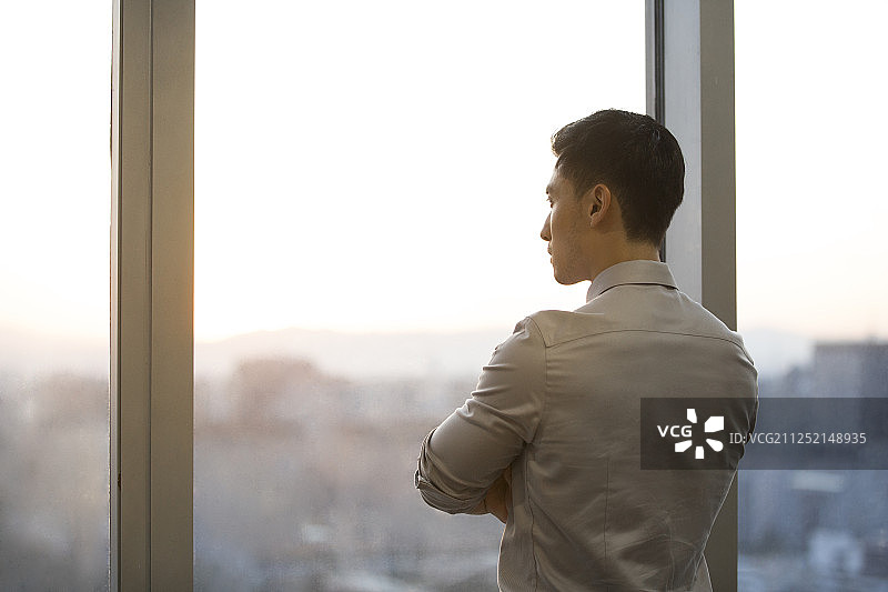 一个成功男商务人士站在办公大厦玻璃窗前思考看向窗外风景图片素材