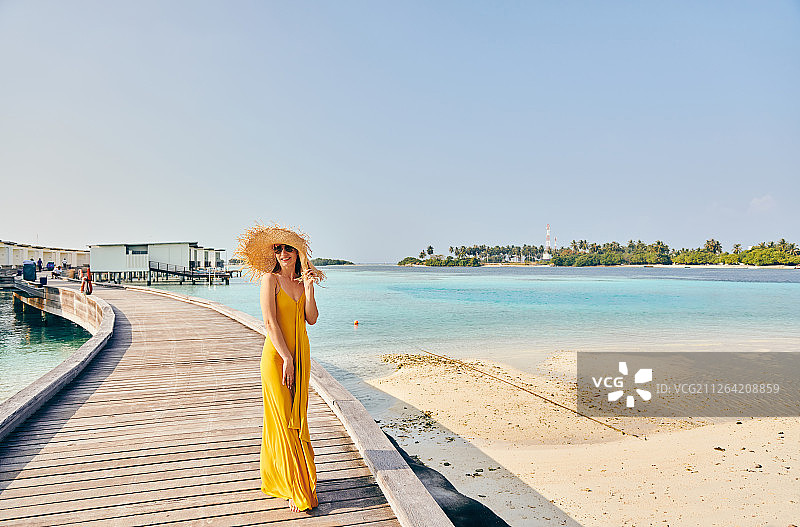 穿着裙子的女人走在热带海滩木板路上。暑假在马尔代夫。图片素材