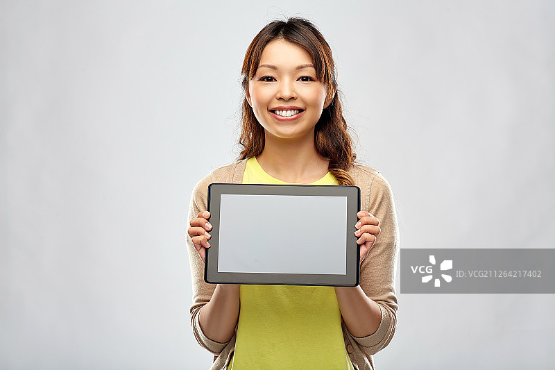 科技和人的概念-快乐的亚洲女人显示平板电脑在灰色的背景。快乐的亚洲女人展示平板电脑图片素材