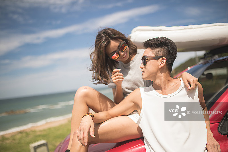 一对夫妇戴着太阳镜倚靠在停在海滩上的汽车上的照片图片素材