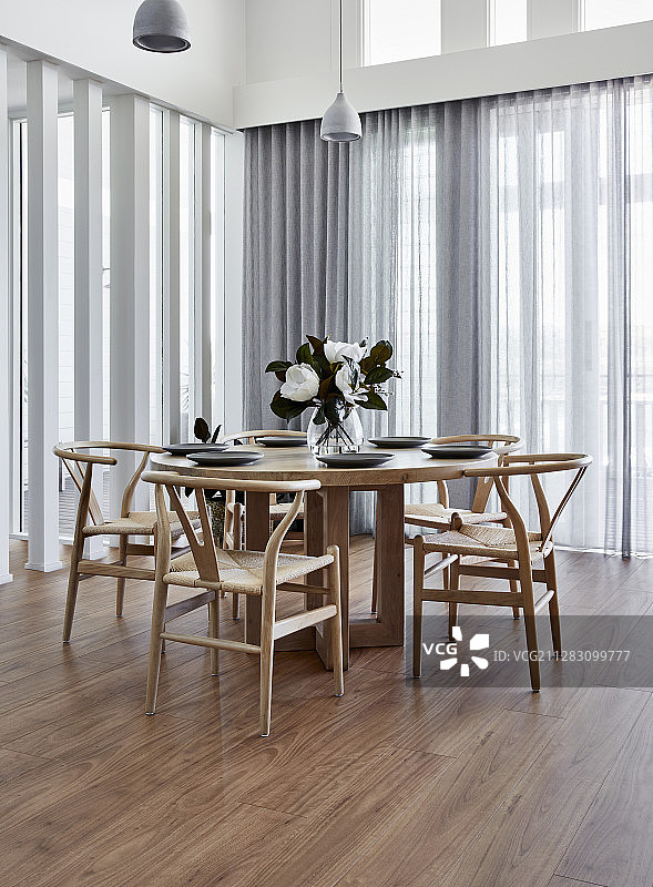 设计师椅子放在圆形木桌旁，周围是玻璃幕墙和半透明的窗帘图片素材