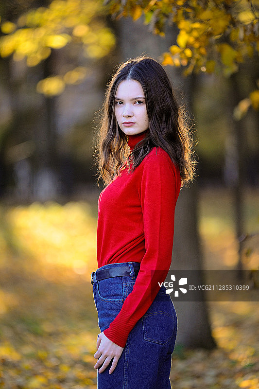 一名穿着红色衬衫和牛仔裤的黑发女子的肖像，站在一棵黄色的树下，秋天，波多尔斯克，莫斯科州，俄罗斯图片素材