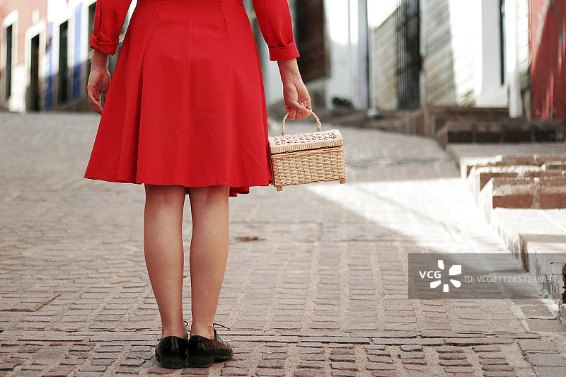 墨西哥瓜纳华托，一名身穿红色裙子的女子下半身挎着篮子站在砖路上图片素材